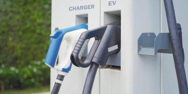 Hand pulling in cable from EV car charger or electric vehicle station. Cable connected at gas station, power supply battery charging an alternative eco environment future technology energy innovation